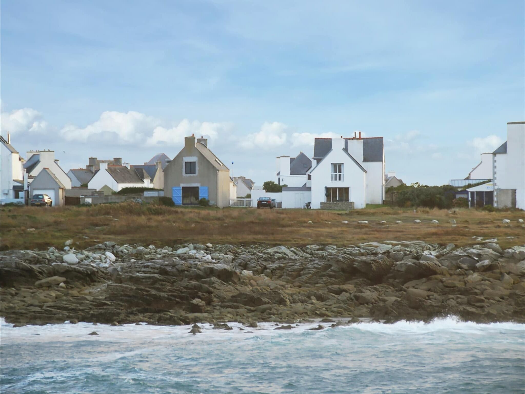 Un village côtier aux maisons blanches, avec un rivage rocheux et des vagues qui déferlent sur la plage.