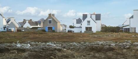 Un village côtier aux maisons blanches, avec un rivage rocheux et des vagues qui déferlent sur la plage.