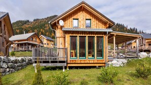 A wooden chalet with a balcony, large windows, and a stone wall in a mountainous area. - Chalet in Hohentauern in the ski area (Hohentauern)