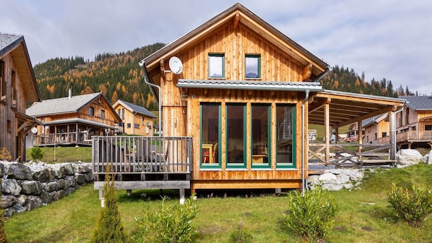 Eine Holzhütte mit Balkon, großen Fenstern und einer Steinmauer in einer Berglandschaft.