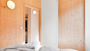 Ein Schlafzimmer mit Holzbalkendecke, einem Bett mit weißer Bettwäsche, einer runden Leuchte und einer Tür zu einem Badezimmer.