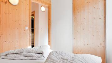 Une chambre avec un plafond en bois, un lit avec une literie blanche, un luminaire rond et une porte donnant sur une salle de bain.