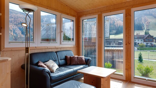 A wooden interior with a black leather sofa, a wooden table, and large windows offering a view of a mountainous landscape. - Chalet in Hohentauern in the ski area (Hohentauern)