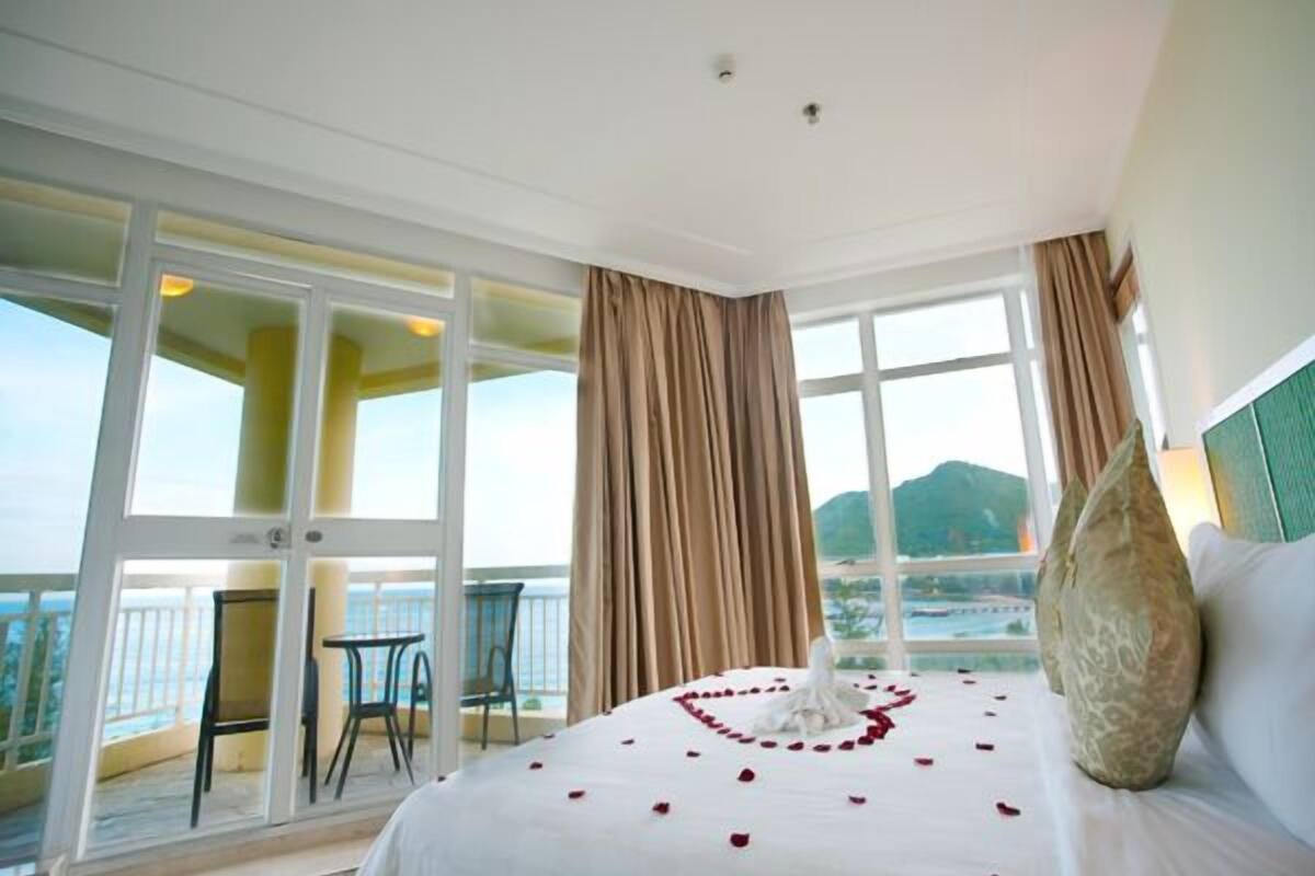 Una habitación de hotel con una cama grande, un balcón con sillas y vistas panorámicas.