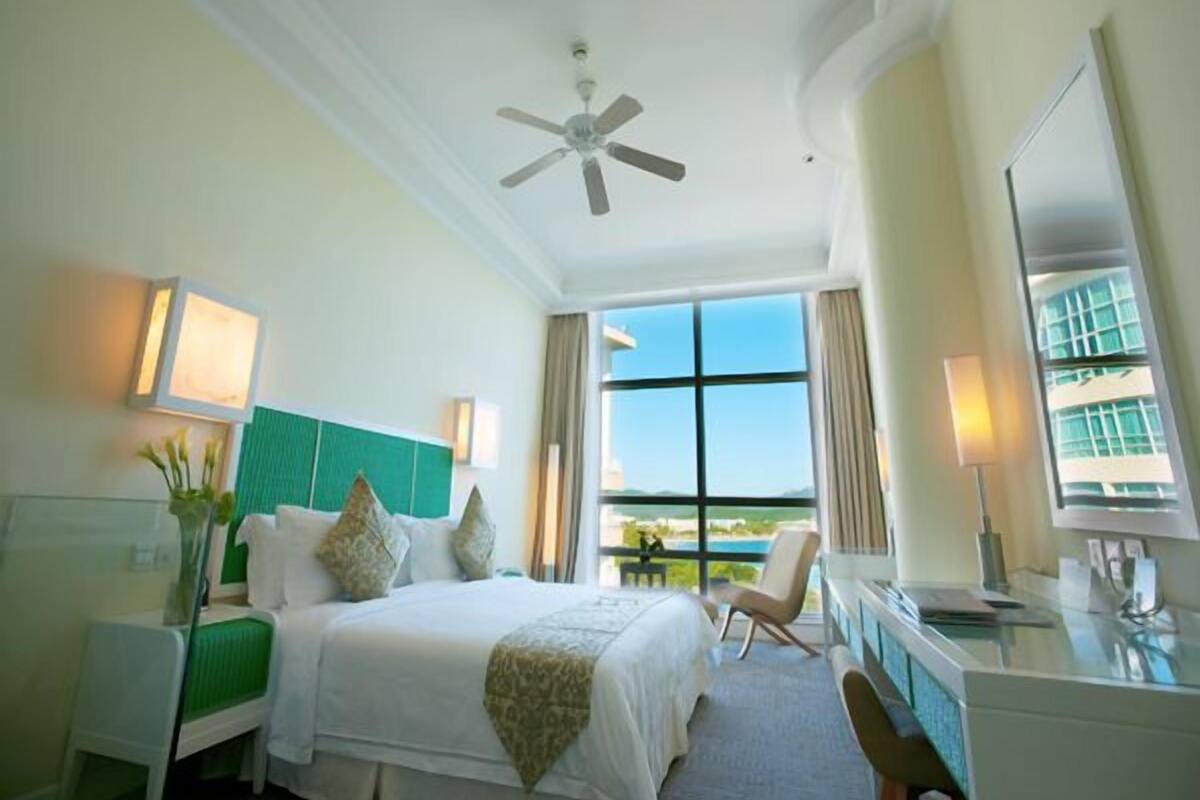 Habitación de hotel con cama, escritorio, silla, ventilador de techo y una ventana grande con vistas.