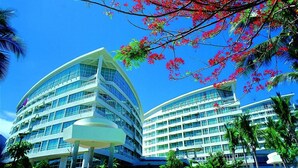 Un hotel moderno con fachada curva, varios balcones y abundante vegetación en primer plano.