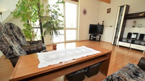 A living room with a wooden coffee table, two patterned sofas, a television, a potted plant, and a cabinet with kitchenware. - South Bohemia Family Escape (Bechyne)