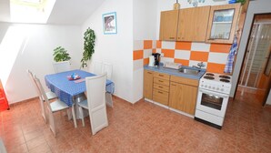 A compact kitchen with a dining area, featuring a tiled floor, wooden cabinets, a stove, and a small table with chairs. - South Bohemia Family Escape (Bechyne)