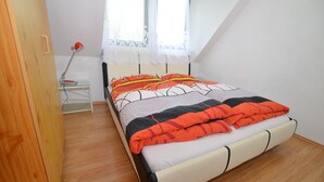A bedroom with a bed, a nightstand, a lamp, and a window with lace curtains. - South Bohemia Family Escape (Bechyne)