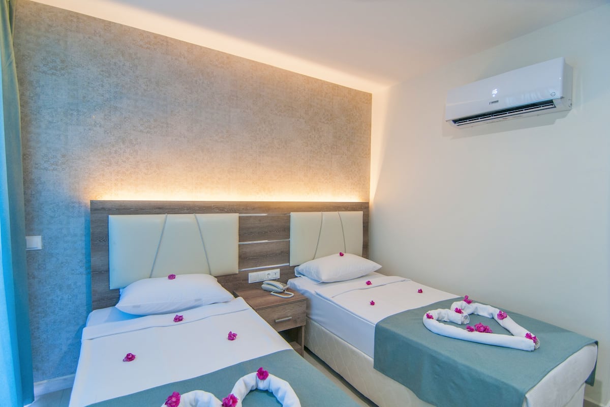 A hotel room with two beds, a wooden headboard, an air conditioner, and a bedside table with a phone.