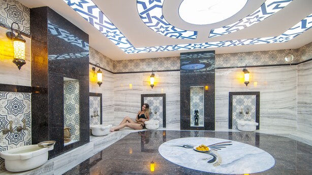 Een luxe badkamer met een ronde marmeren vloer in het midden, decoratieve wandtegels en meerdere verlichtingsarmaturen.