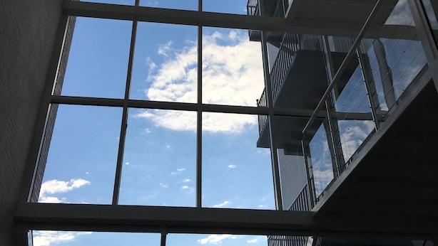 A view through a large window with a grid pattern, revealing a clear sky with clouds and a building with a sloped roof in the background. - SmartHotel Flamingo self-check-in (Giessen)
