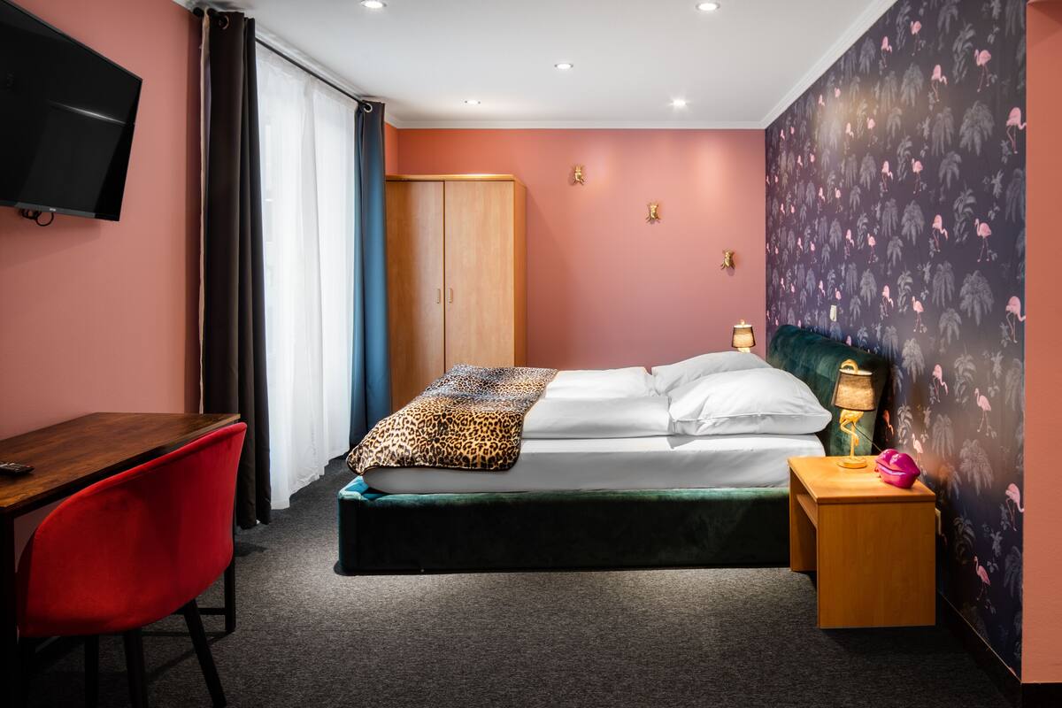 A bedroom with a bed, a desk, a chair, a TV, and a nightstand.