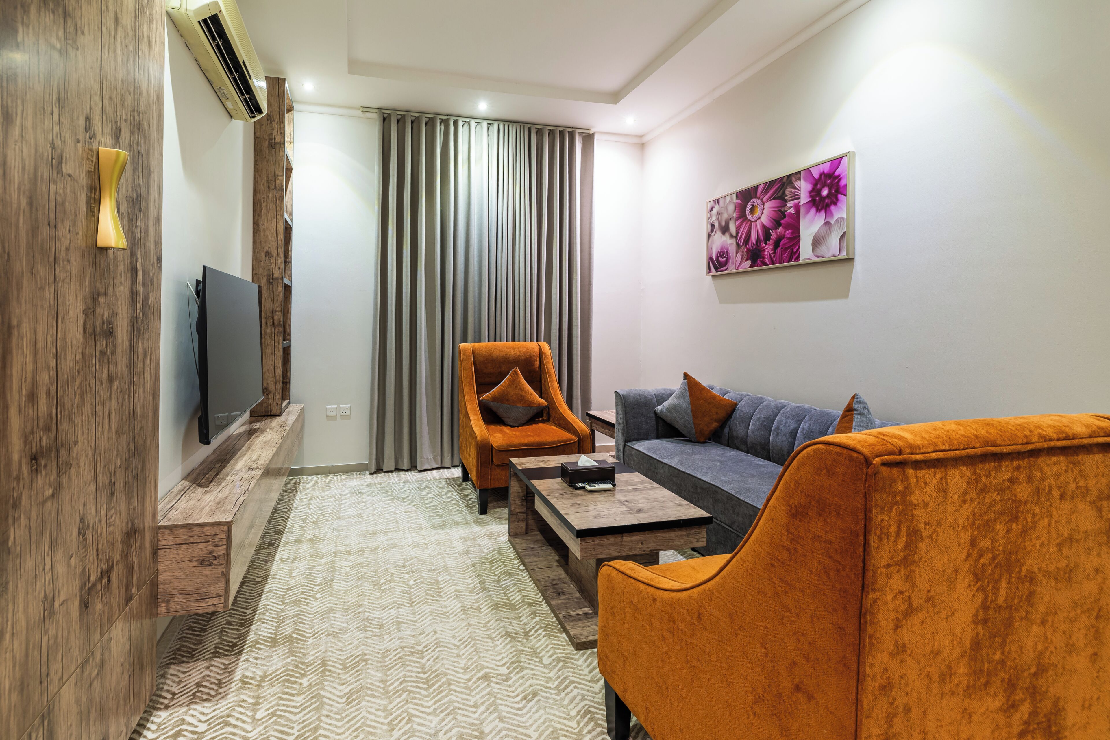 A modern living room with a sofa, armchair, and a flat-screen TV mounted on a wooden panel.
