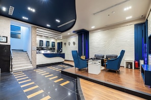 Un hall d’entrée moderne avec un comptoir d’accueil, des chaises bleues, un escalier et un mur décoré de motifs.