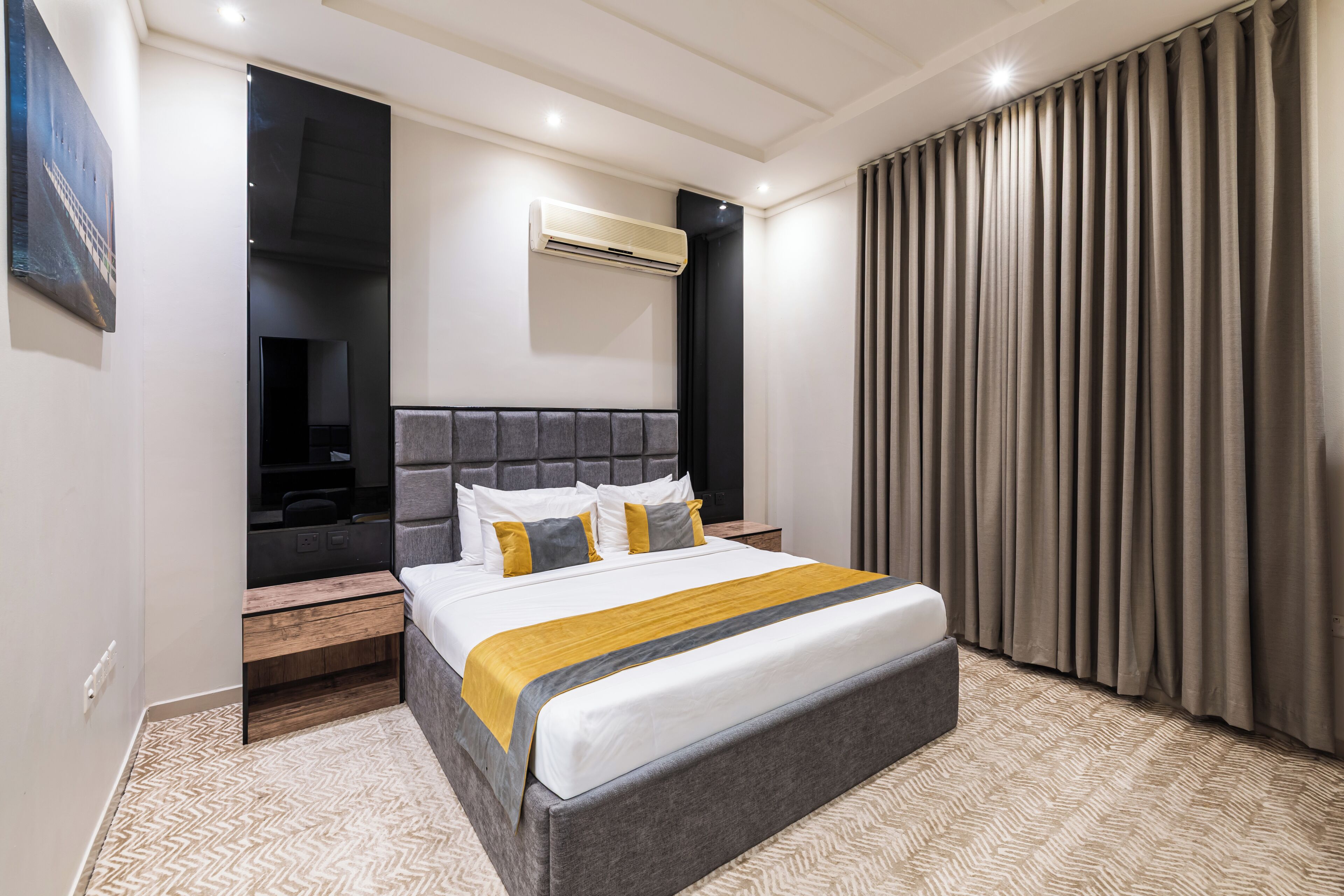 A modern hotel room with a large bed, a flat-screen TV, a built-in bench, and a large window with curtains.