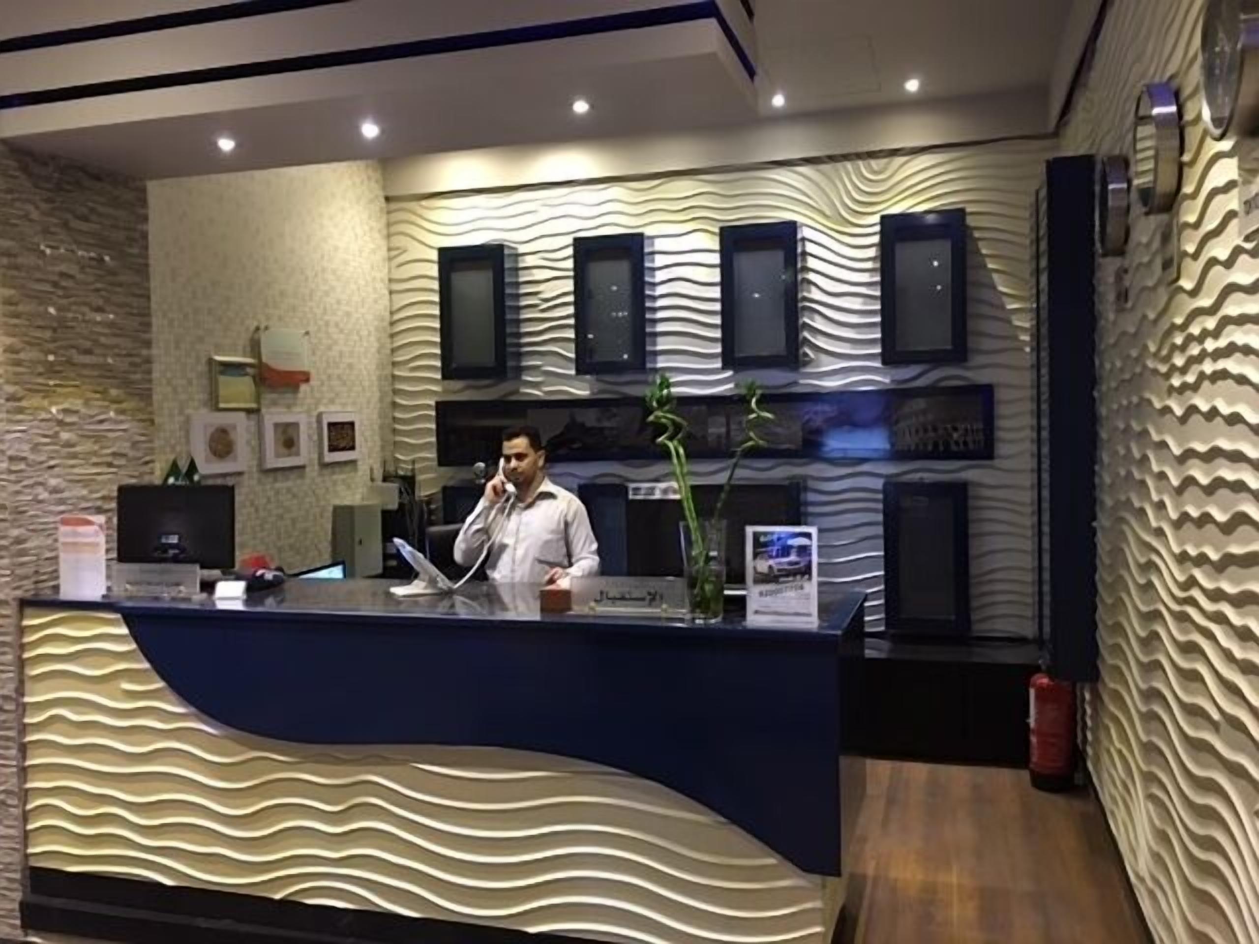 A reception desk with a wavy design, a man standing behind it, and a wall with a textured pattern and framed pictures.