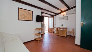 A room with a wooden ceiling, a white sofa, a wooden table with chairs, and a television mounted on the wall. - Terrazza Bordonaro (Cefalù)