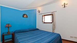 A bedroom with a bed, a nightstand, a lamp, a window with curtains, and wall sconces. - Terrazza Bordonaro (Cefalù)