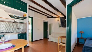 A compact kitchen with a dining area, a small table with a wine glass, and a bed in the adjacent room. - Terrazza Bordonaro (Cefalù)