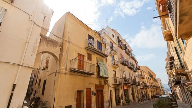 A narrow street with buildings featuring balconies and a cobblestone road. - Terrazza Bordonaro (Cefalù)