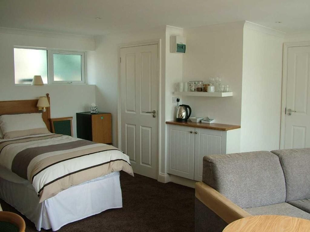Camera d'albergo con un letto, una poltrona, un tavolino, un mobiletto con accessori da cucina e una finestra.