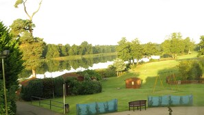 A serene park with a lake, a wooden cabin, and a swing set. - Gosfield Lake Resort (Halstead)