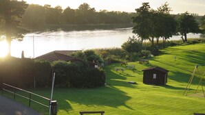 A lakeside view with a grassy area, picnic tables, a small cabin, and a metal fence. - Gosfield Lake Resort (Halstead)