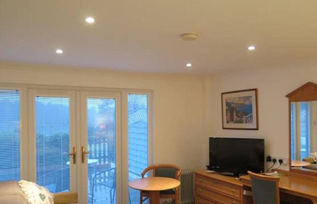 A room with a television, a chair, a desk, and a window with blinds.