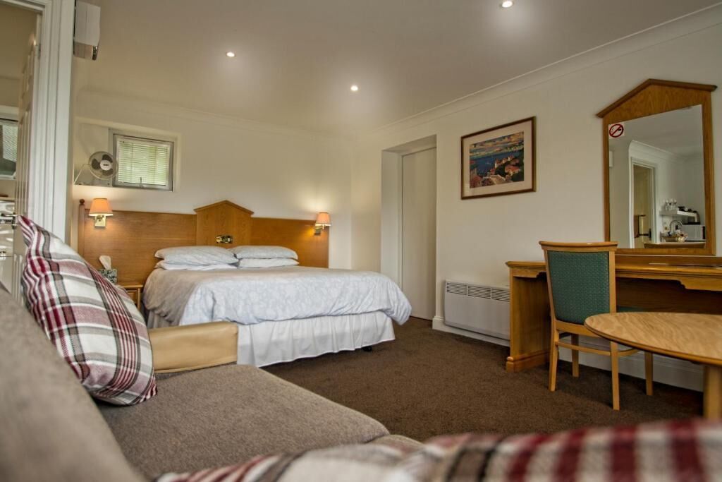 A hotel room with a bed, a desk, a chair, a sofa, a mirror, and a picture on the wall.