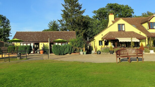 A yellow building with a brown roof, a bench in the foreground, and a well-maintained lawn. - Gosfield Lake Resort (Halstead)