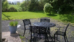 An outdoor seating area with a round table and four chairs, surrounded by greenery and a grassy field. - Lisnafillan Lodge (Ballymena)