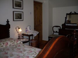 Un dormitorio con cama, mesita de noche, cómoda, silla y puerta de madera.