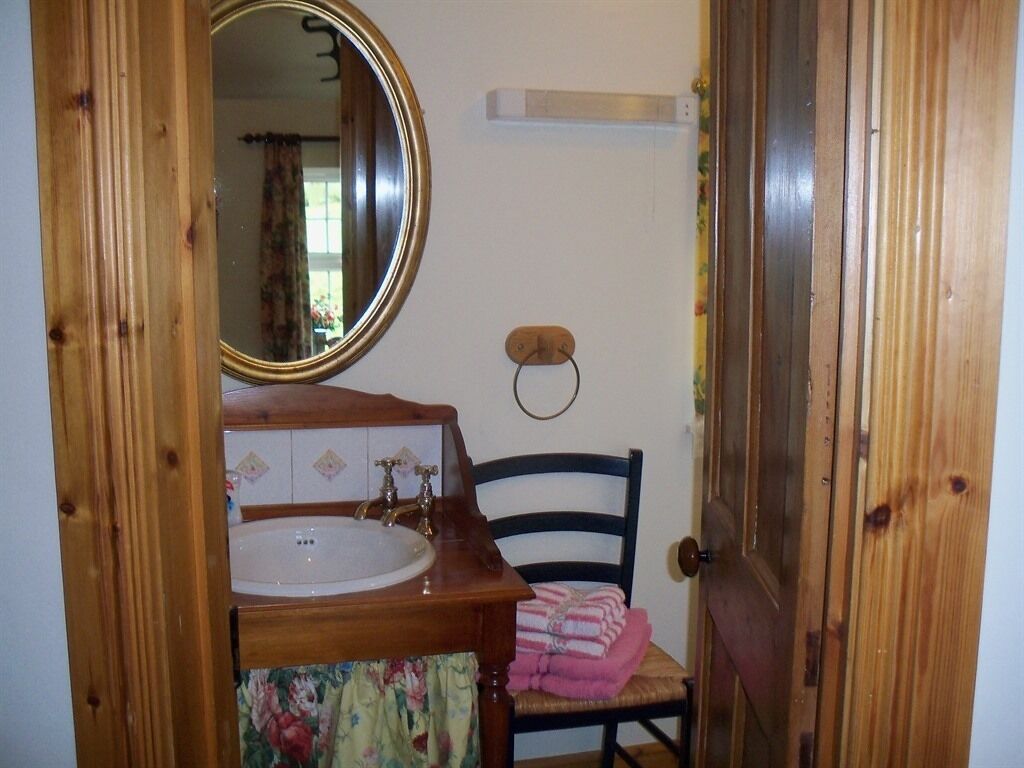 A bathroom with a wooden vanity, a round mirror, and a chair with a towel.