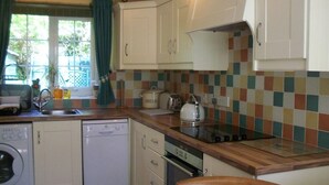 A compact kitchen with white cabinets, a dishwasher, an oven, and a tiled backsplash. - Lisnafillan Lodge (Ballymena)