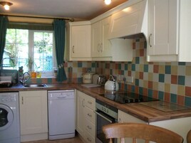 Una cocina compacta con armarios blancos, lavavajillas, horno y salpicadero de azulejos.