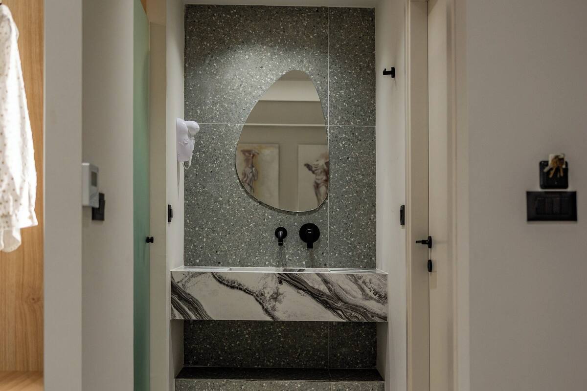 A modern bathroom with a marble sink, a large mirror, and a speckled backsplash.
