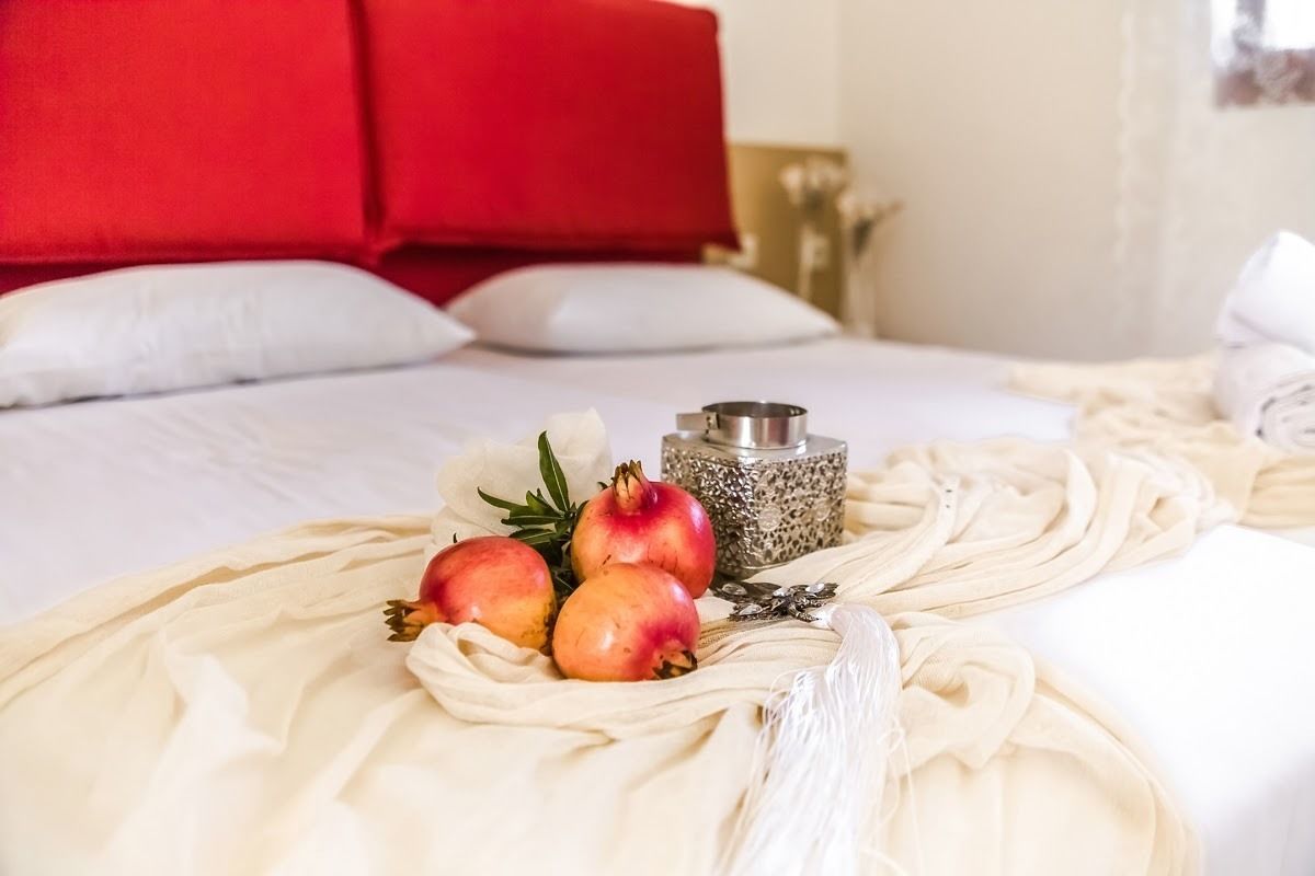 A neatly made bed with white linens, a red headboard, and a decorative arrangement of pomegranates and a candle on the bedspread.