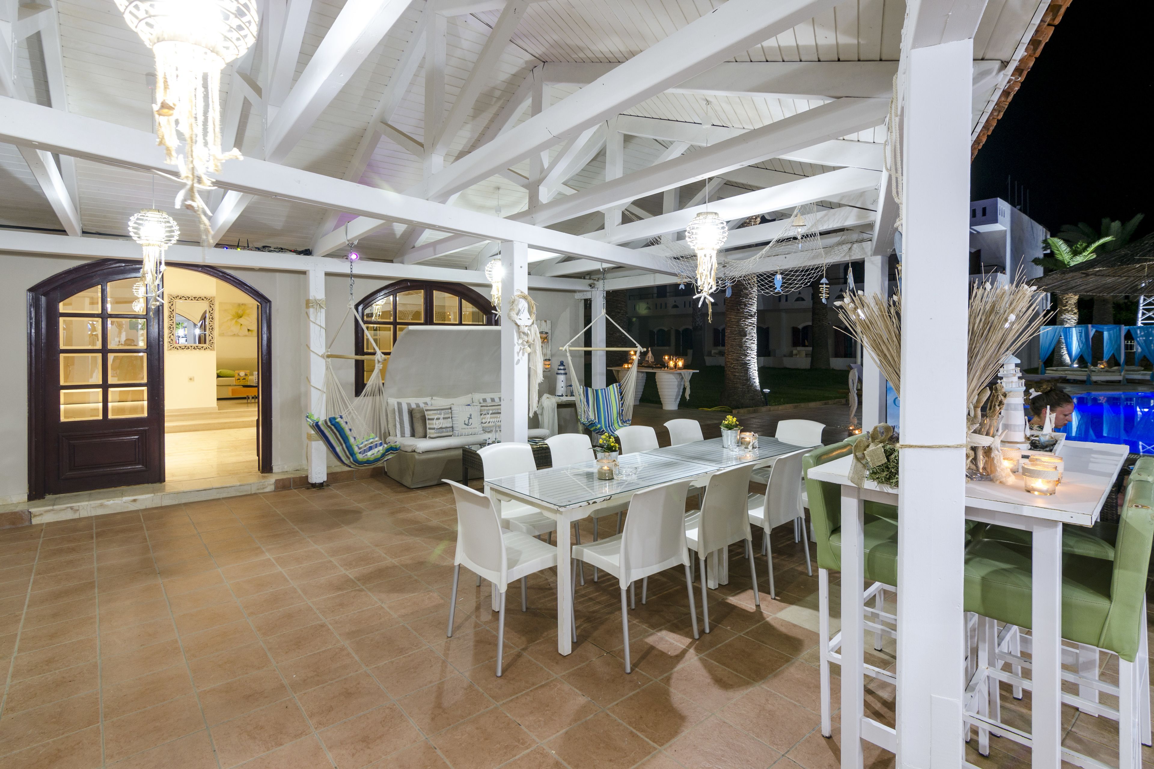 An outdoor dining area with white tables and chairs, a hammock, and a pool in the background.