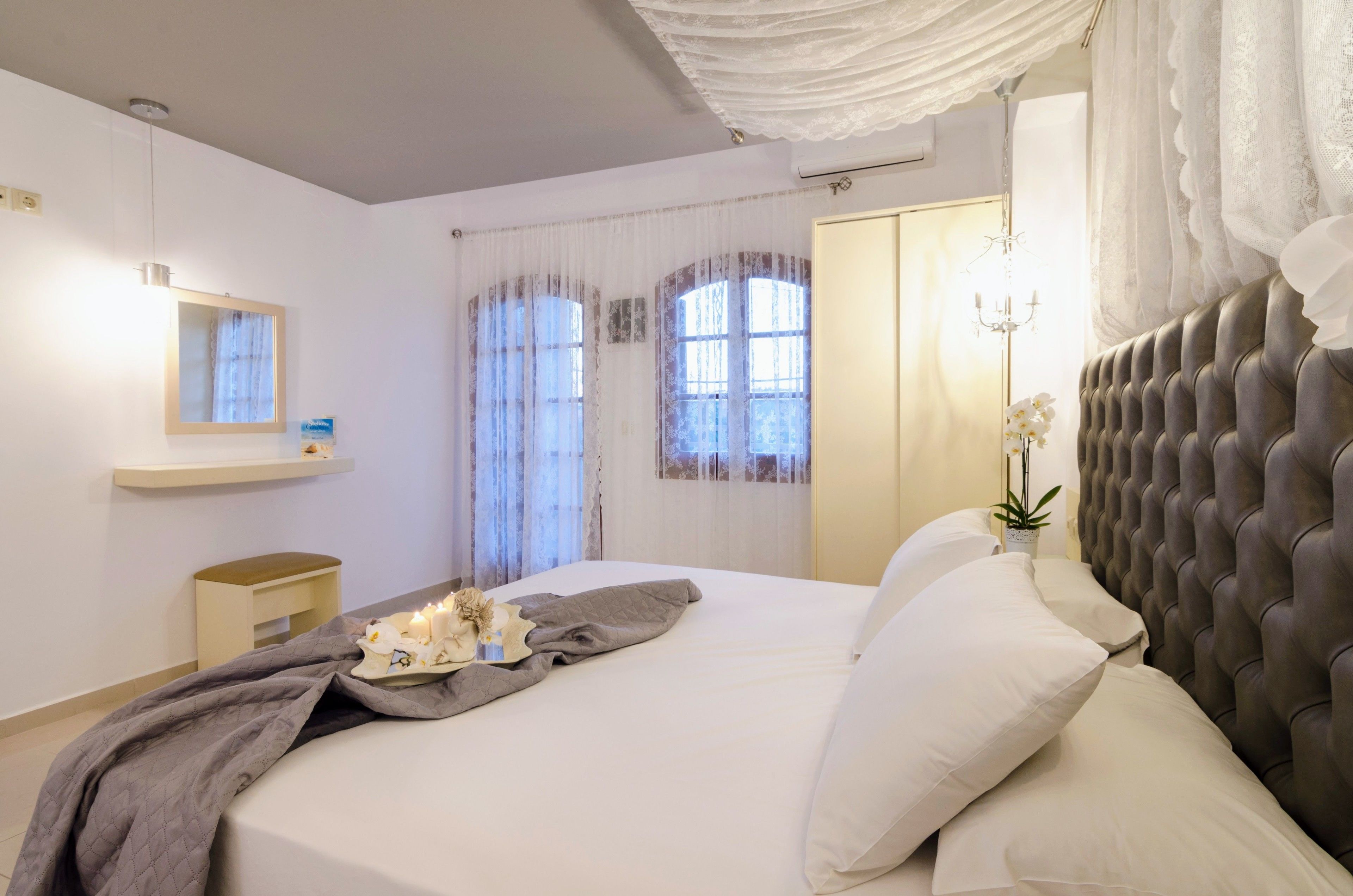 A modern bedroom with a large bed, a bedside table, a mirror, and a window with curtains.