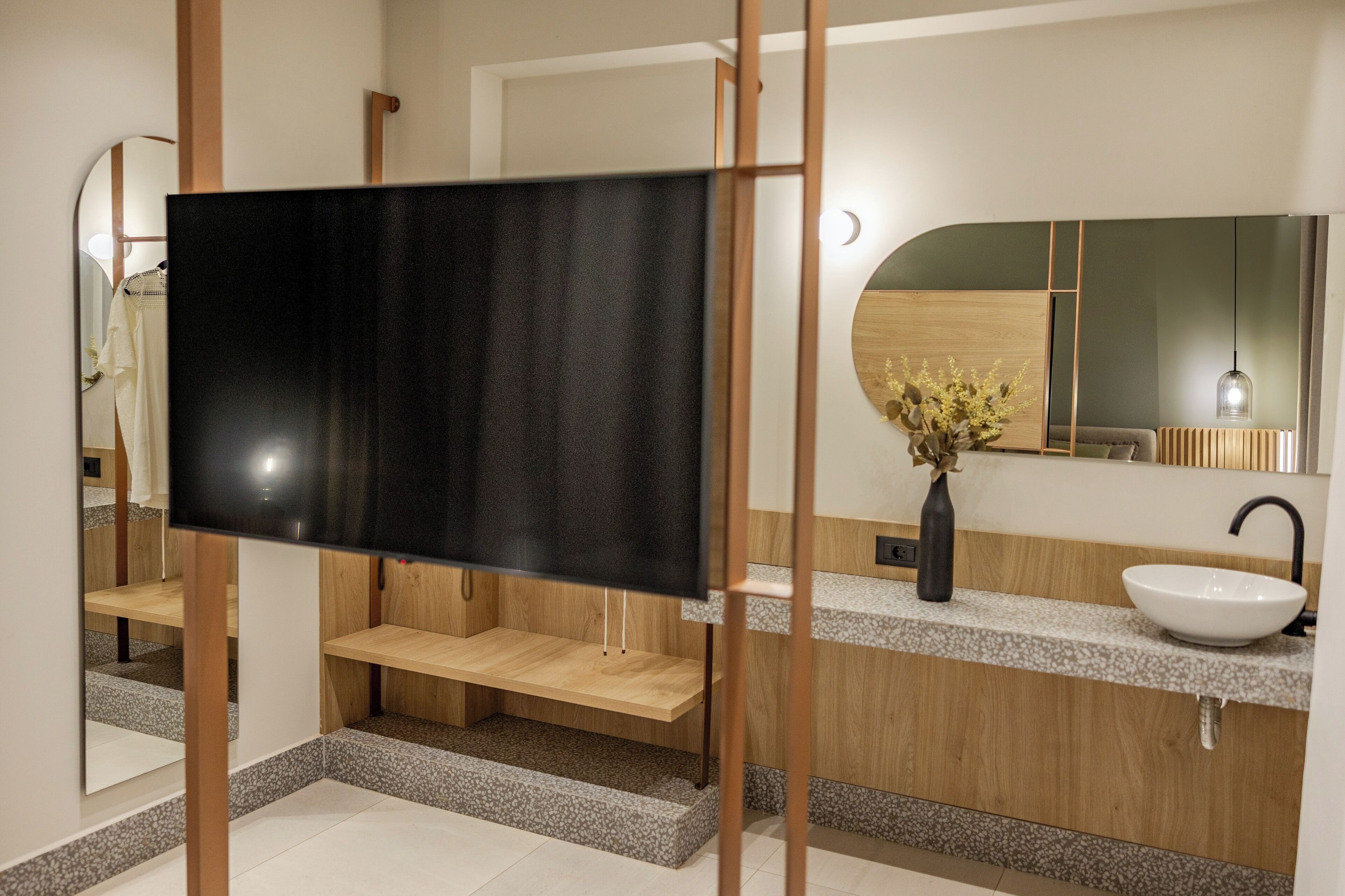 A modern bathroom with a wooden vanity, a white sink, a mirror, and a black screen.