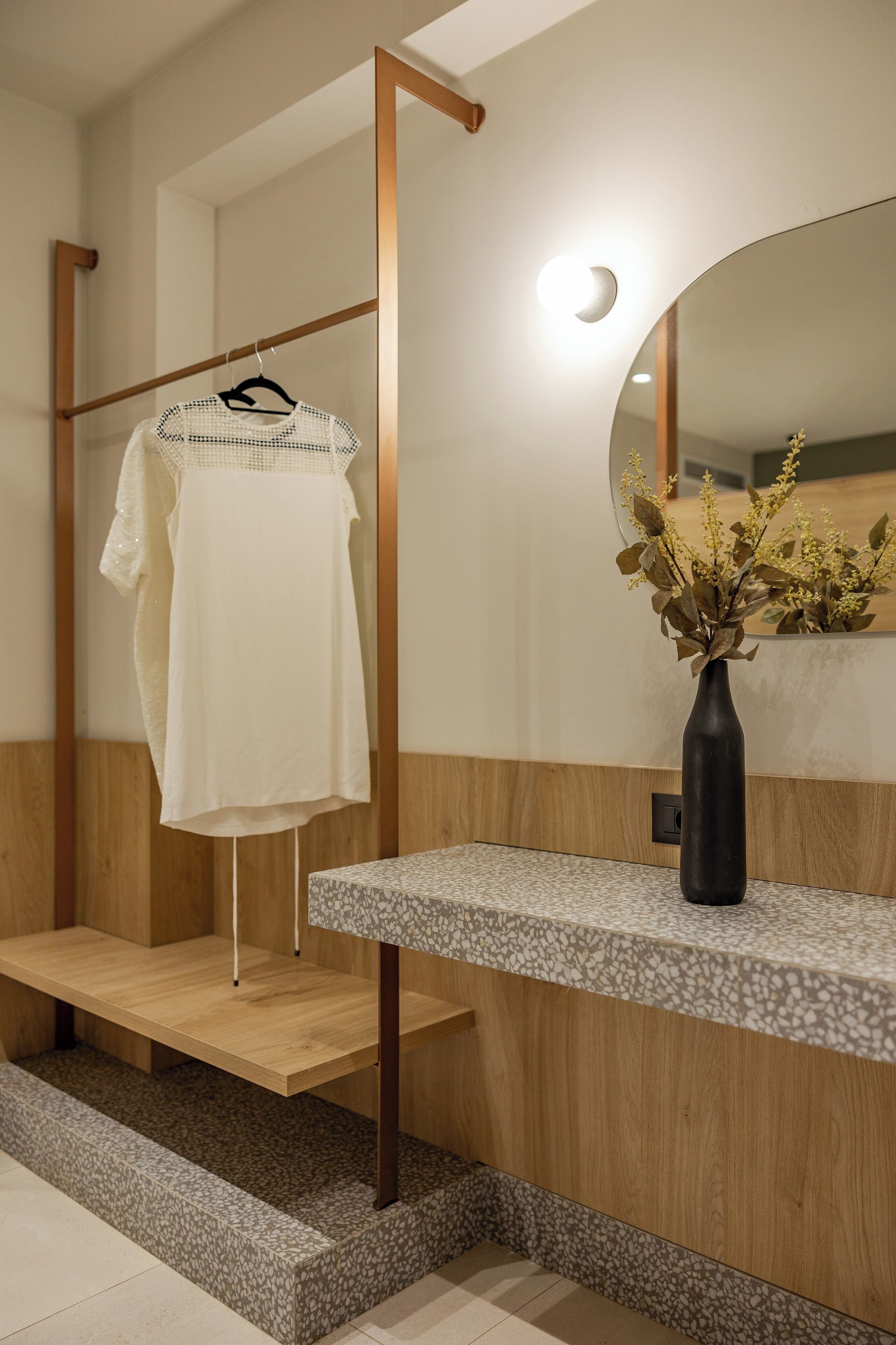 Un baño moderno con tocador de madera, bata colgada y un florero con flores secas.