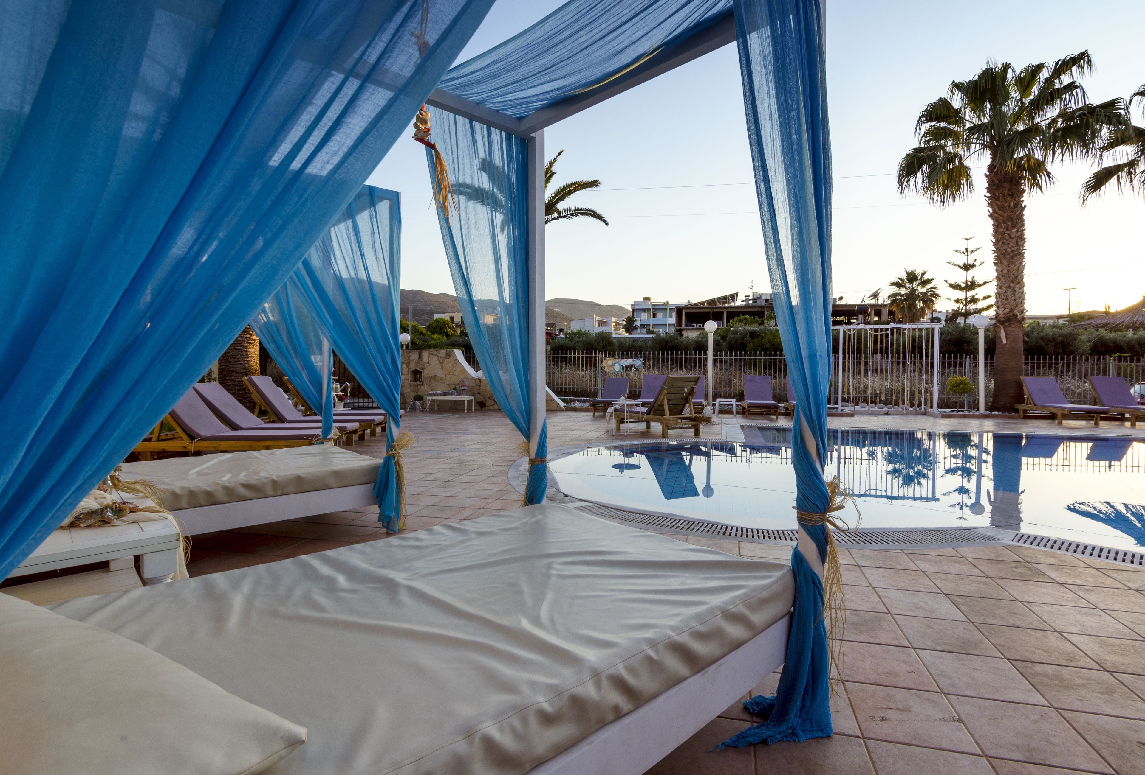 Zona junto a la piscina con una cama, sillones reclinables y vista despejada a la piscina.