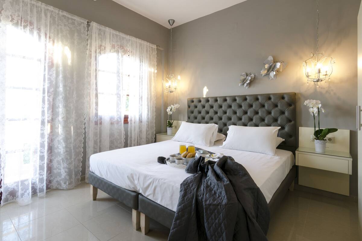A neatly made bed with pillows, a bedside table with a plant, and a tray with breakfast items.