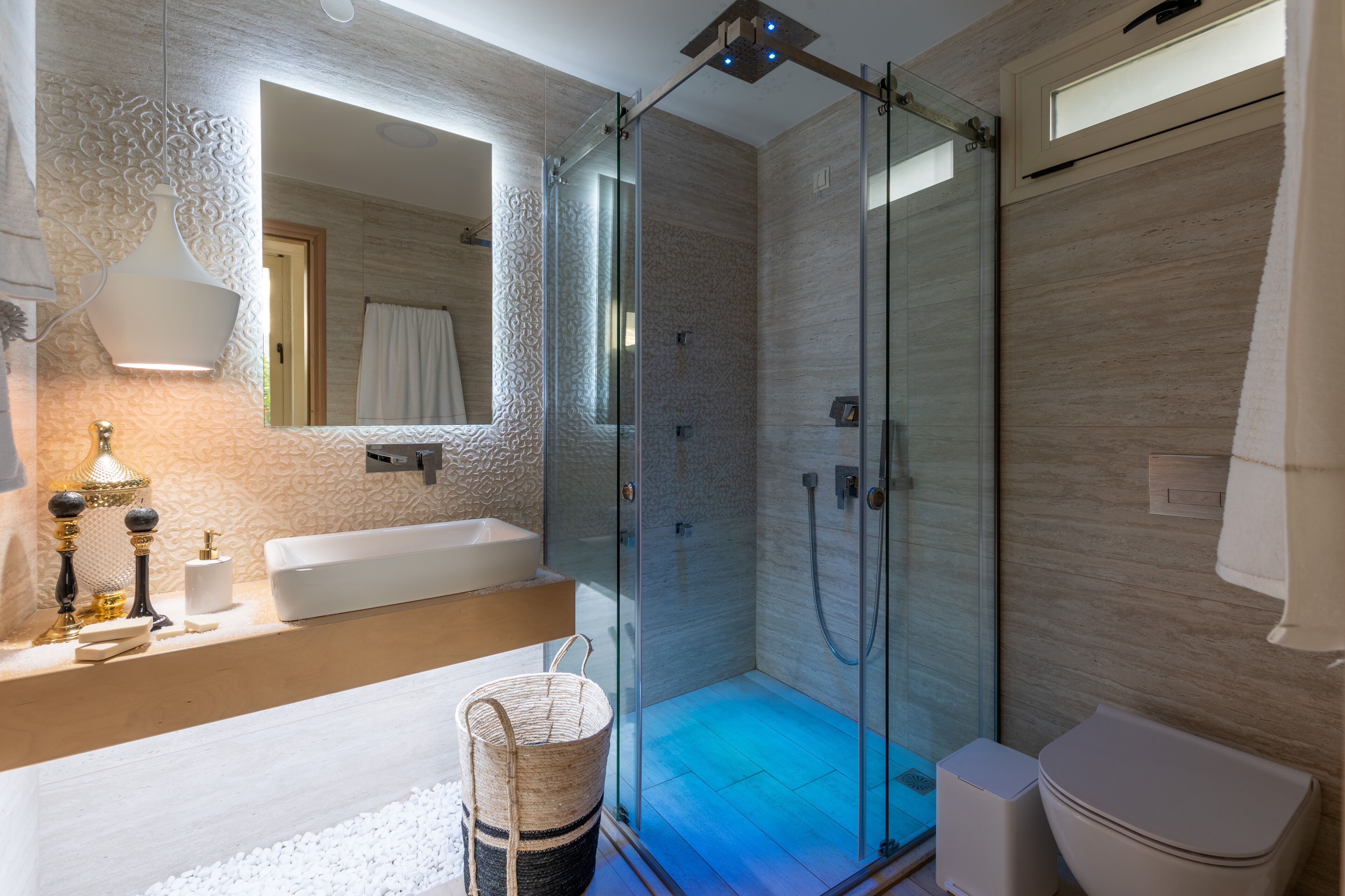 Un baño moderno con ducha envuelta en vidrio, un espejo grande y un lavamanos blanco.