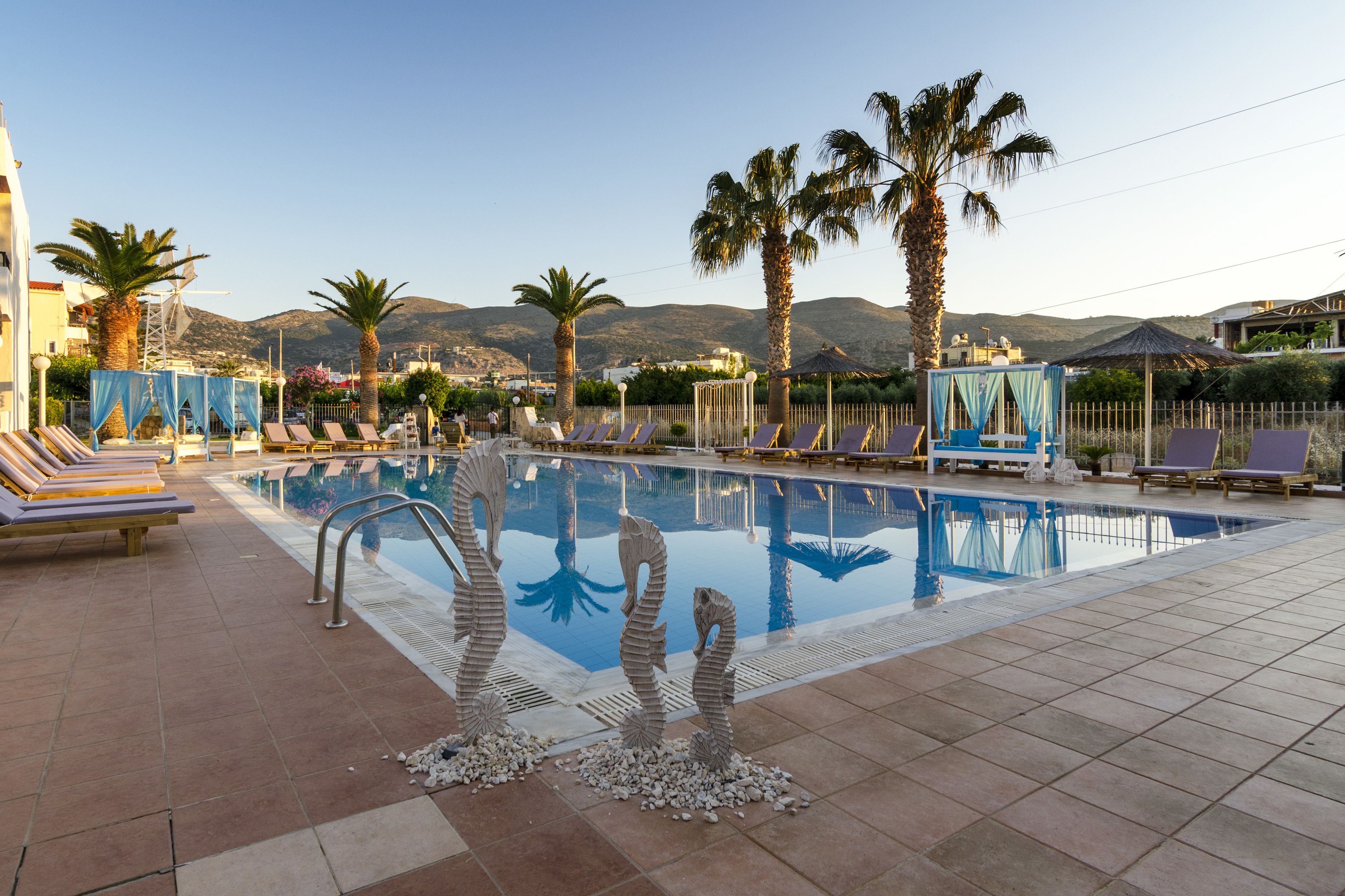 A swimming pool with lounge chairs and palm trees, surrounded by mountains.