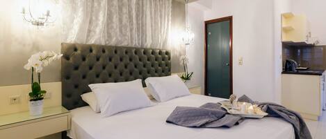 A neatly made bed with white linens, a tufted headboard, and a bedside table with a vase of white flowers.