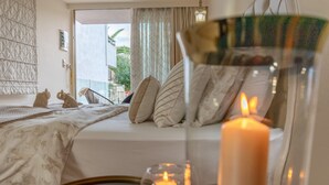 Un dormitorio con cama, almohadas, una mesita de noche con una vela y vistas al exterior.