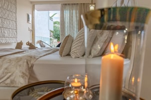 Un dormitorio con cama, almohadas, una mesita de noche con una vela y vistas al exterior.