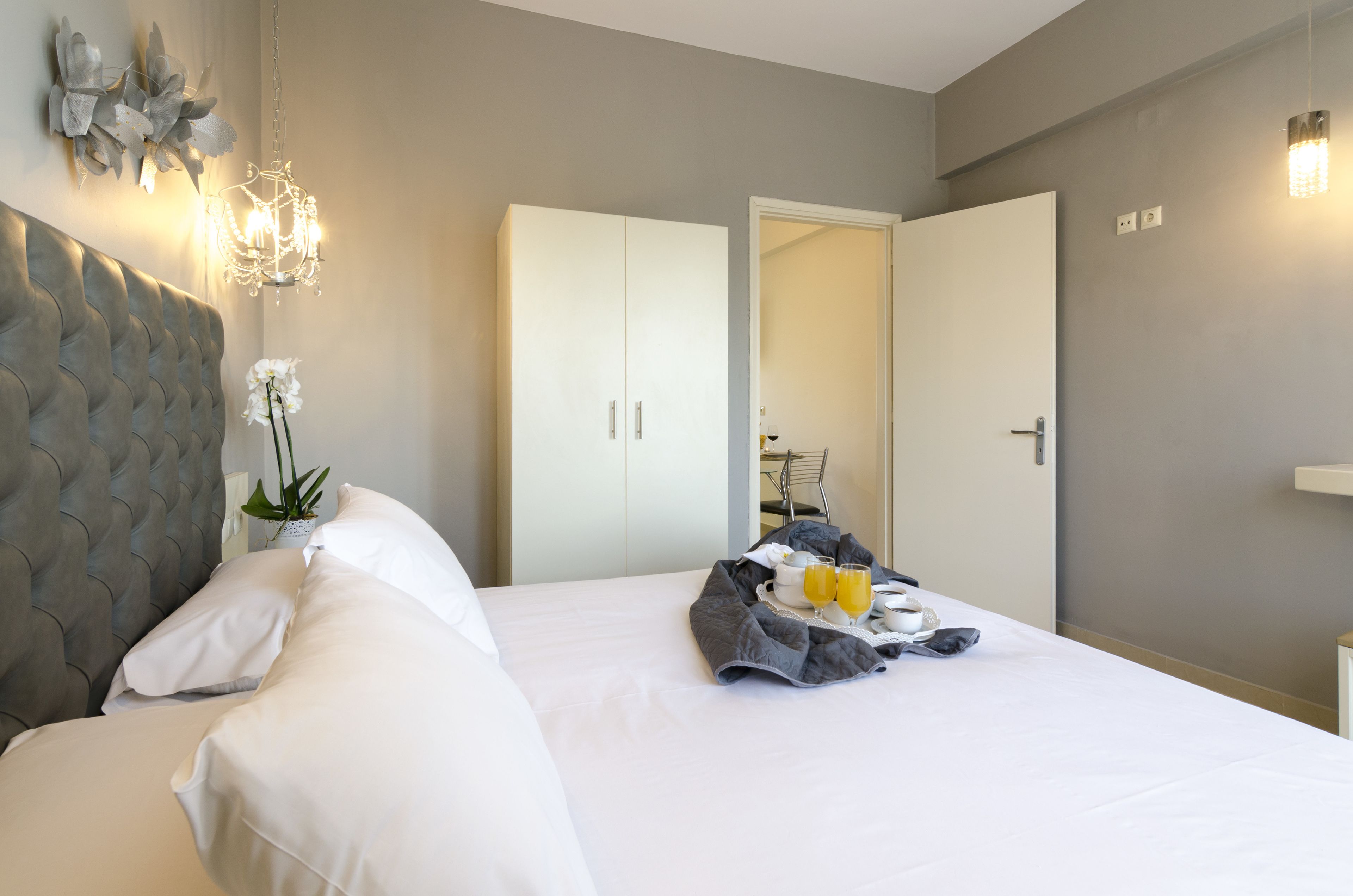 A hotel room with a large bed, a chandelier, a wardrobe, and a breakfast tray with orange juice.